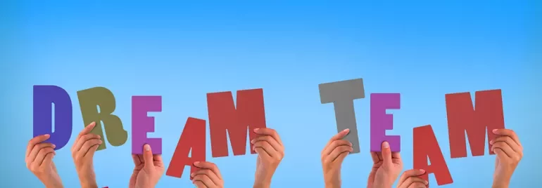 Ręce trzymające litery tworzące napis 'dream team' na tle nieba.