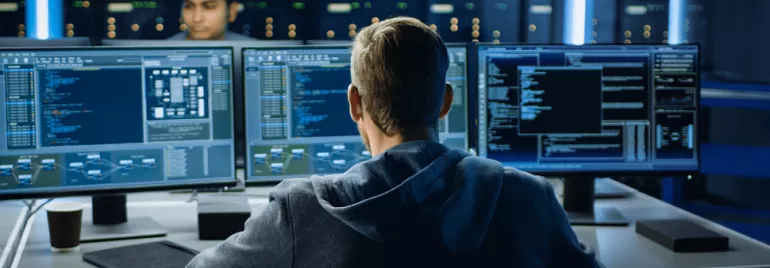 Man working at multi-monitor setup in a server room.