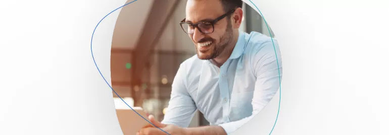 Smiling man in glasses using a laptop indoors.