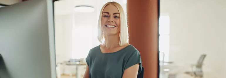Uśmiechnięta kobieta przy biurku w nowoczesnym biurze.