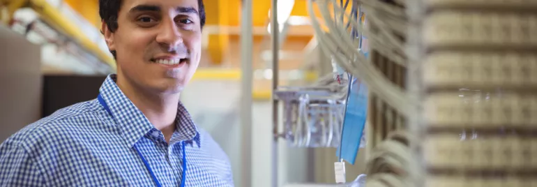 Man in a checkered shirt smiling near server cables.