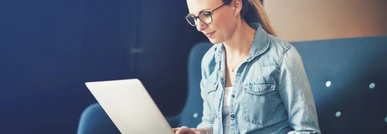 Woman in glasses using a laptop on a couch.