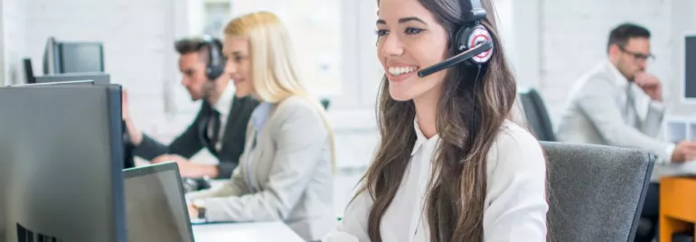 Kobieta z zestawem słuchawkowym uśmiecha się przy komputerze w call center.