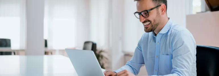 A man sitting down smiling at laptop in front of him