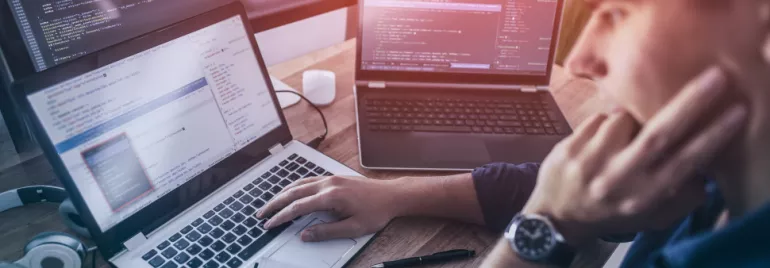 Osoba programująca na laptopie z kilkoma ekranami wyświetlającymi kod.