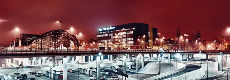 Nocny widok miasta z oświetlonym mostem i nowoczesnymi budynkami.