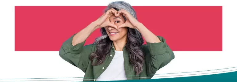 Woman smiling with heart-shaped hands in front of face.