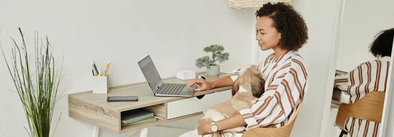 Kobieta pracuje na laptopie w domu z psem na kolanach.
