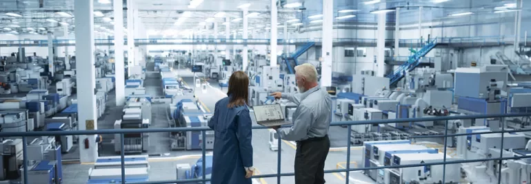 Dwie osoby w fabryce omawiające procesy produkcyjne.