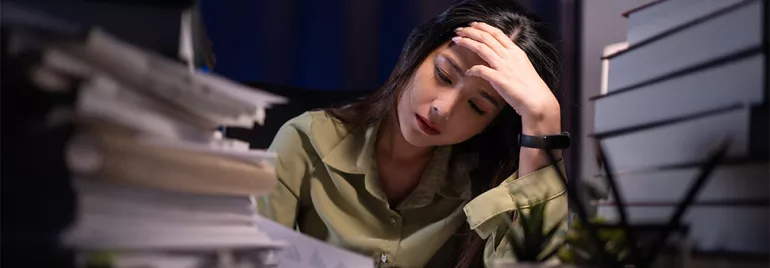 Woman overwhelmed with work at desk covered in papers.