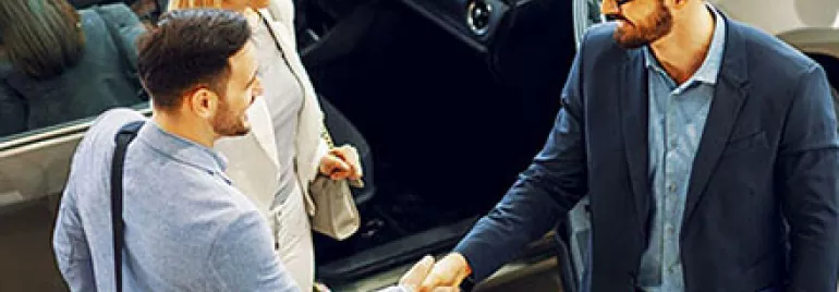Three people shaking hands near a car in a showroom.