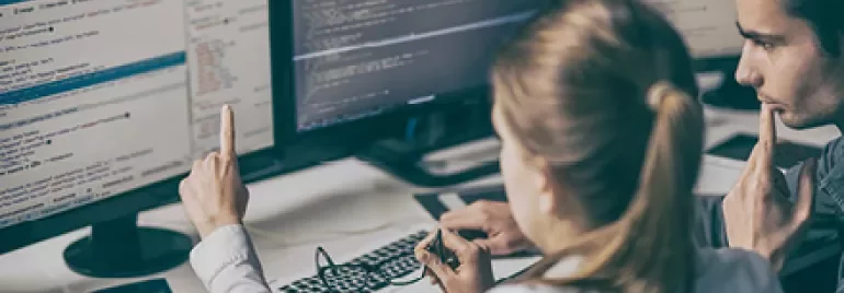 Dwie osoby współpracujące nad kodem z kilkoma ekranami wyświetlającymi programowanie komputerowe.