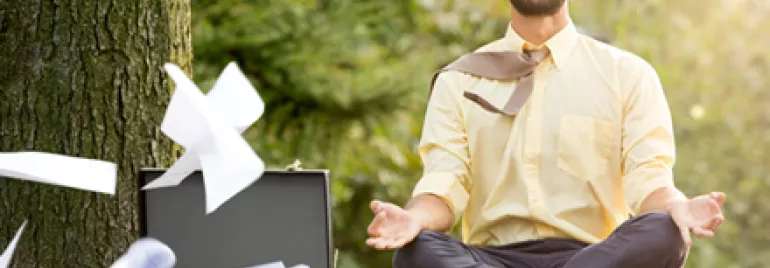 Man meditating outdoors, papers flying from a briefcase