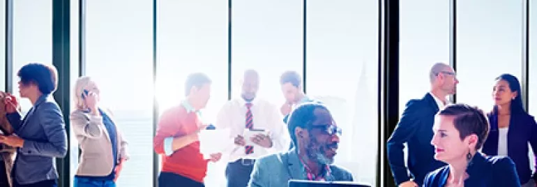 Business people interacting in a bright office with large windows.
