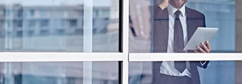Businessman using tablet and phone behind glass window.