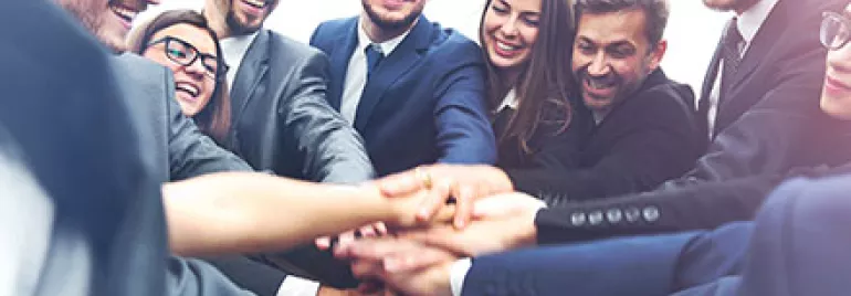 Group of businesspeople joining hands in a circle, smiling.