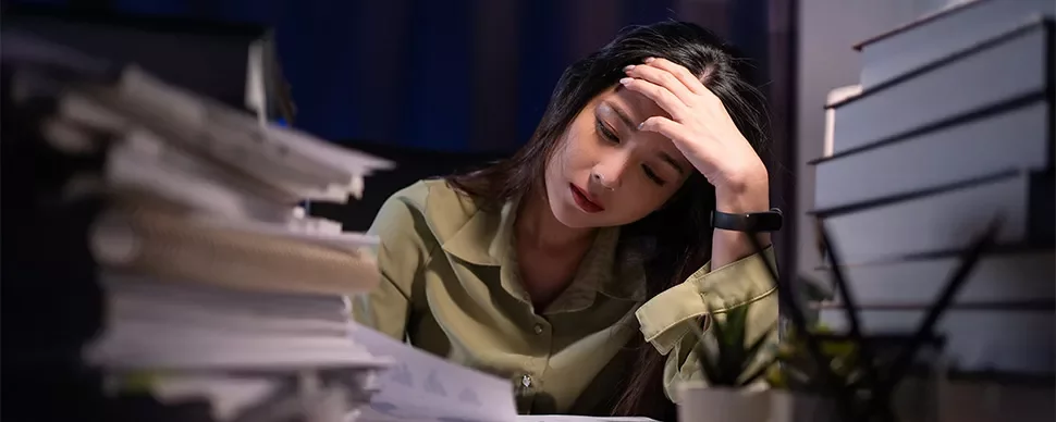 Woman overwhelmed with work at desk covered in papers.