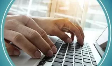 Ręce piszące na klawiaturze laptopa w świetle słonecznym.