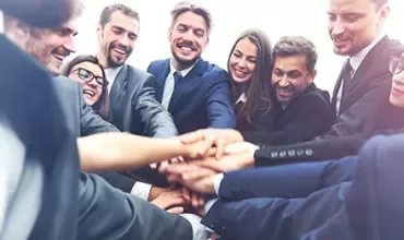 A group of business people in suits putting their hands together in a circle.