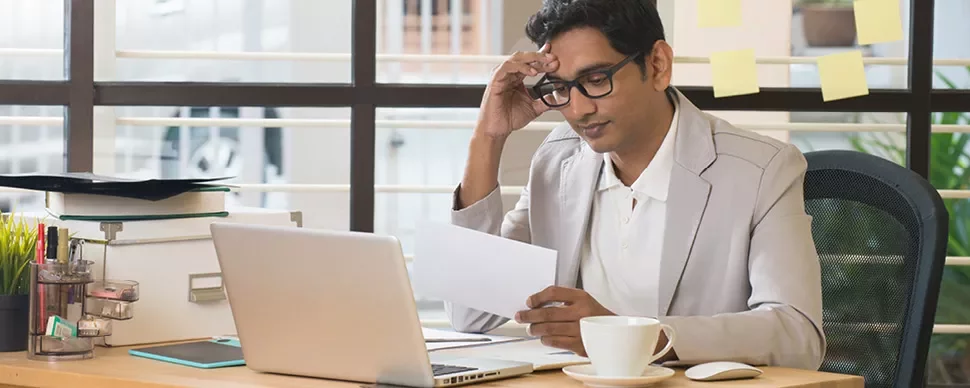 Man in office reading paper with laptop and coffee