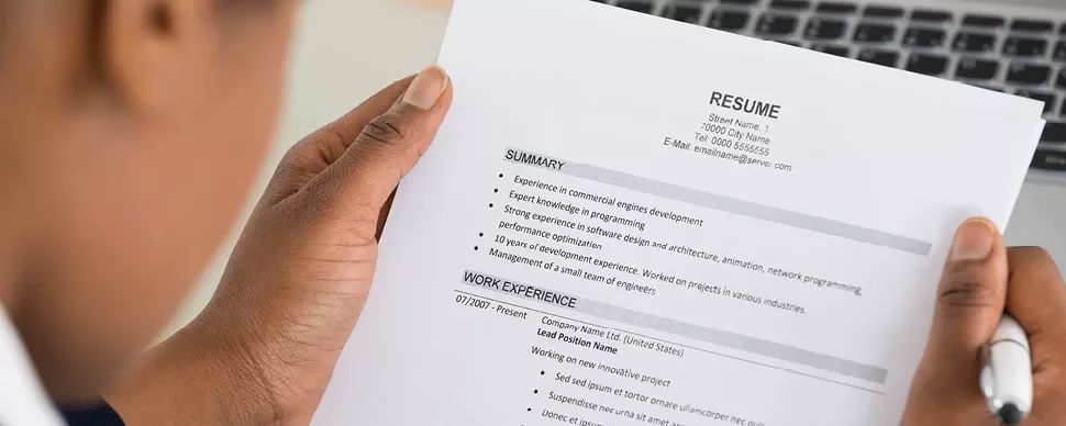 Person reviewing a printed resume with summary and work experience sections visible.