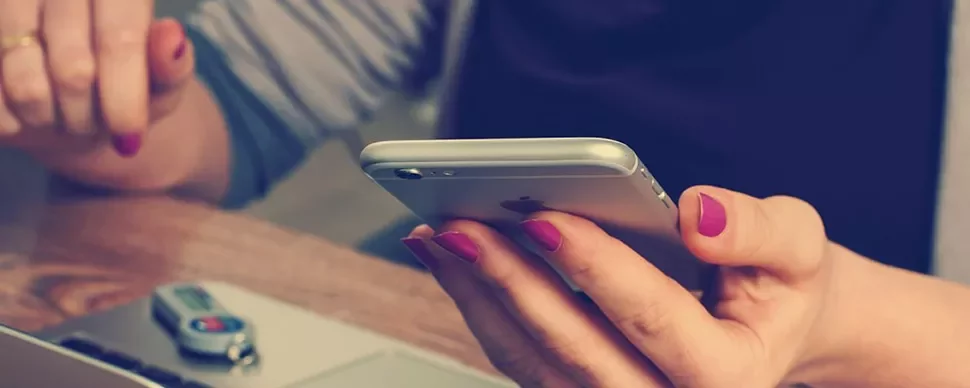 Osoba trzymająca smartfon z laptopem i pendrive'em na stole.