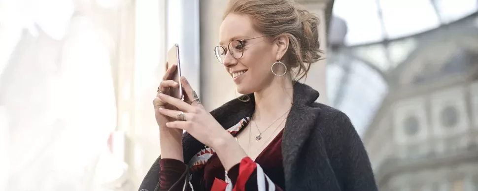 Kobieta uśmiecha się, patrząc na swój smartfon.
