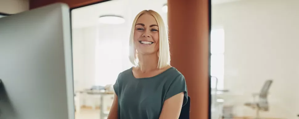 Uśmiechnięta kobieta przy biurku w nowoczesnym biurze.