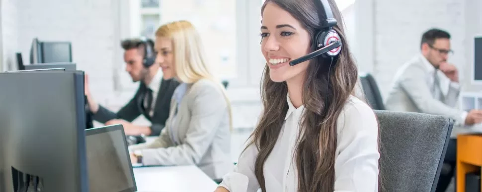 Kobieta z zestawem słuchawkowym uśmiecha się przy komputerze w call center.