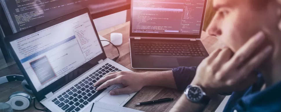 Osoba programująca na laptopie z kilkoma ekranami wyświetlającymi kod.