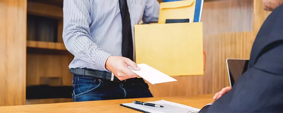  An employee, wearing a shirt and tie, extends a resignation letter to their boss while holding a box of documents.