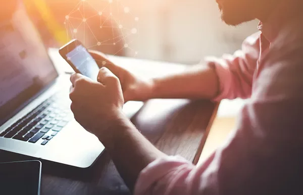 Osoba korzystająca ze smartfona i laptopa przy biurku.