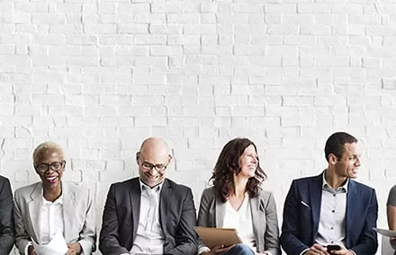 A diverse group of people sitting against a white brick wall.