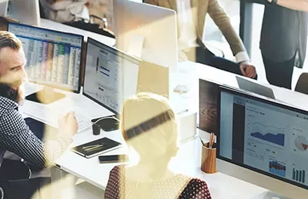 People in an office working at computers with charts displayed on screens.