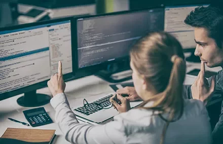 Dwie osoby współpracujące nad kodem z kilkoma ekranami wyświetlającymi programowanie komputerowe.