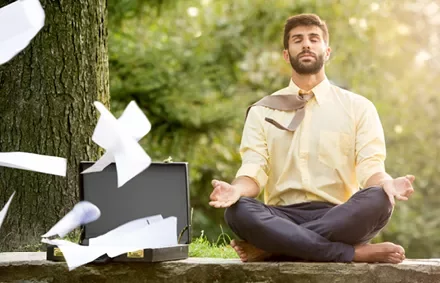 Man meditating outdoors, papers flying from a briefcase