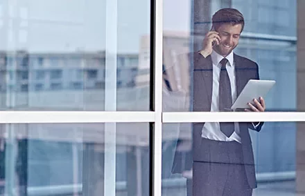 Businessman using tablet and phone behind glass window.